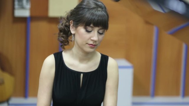 Happy smiling young woman playing grand piano at a concert. Emotional elegant beautiful lady at the stage. Musician plays piano.