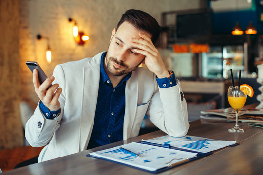 Young Businessman Looking At Phone In Cafe