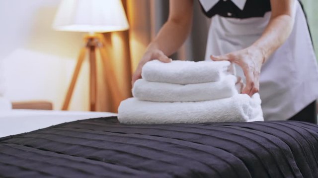 Caucasian middle-aged female chambermaid puttin folded towels on bed in slowmotion