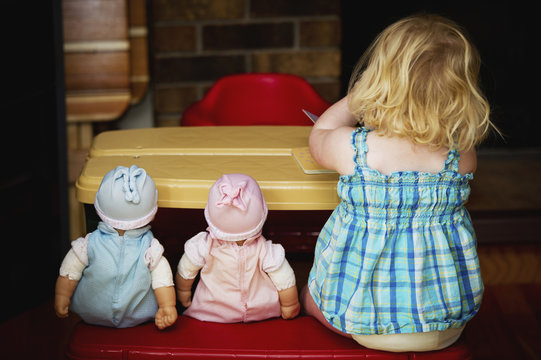 A toddler sits at a play table with her two dolls; Alberta, Canada