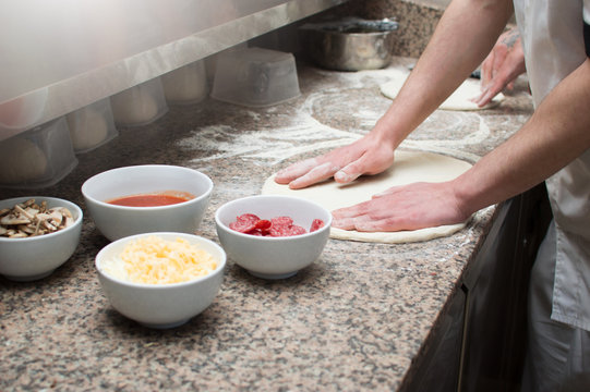 Close-up of male hands baker kneads raw pizza dough. Fast food. Pizza delivery. Baking.