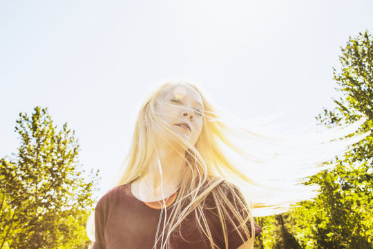 Beautiful young woman listening to music and singing along while swinging her long, blond hair outdoors in a city park; Edmonton, Alberta, Canada