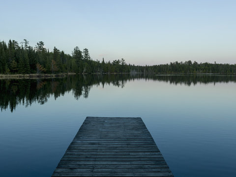 Wooden dock leading out to a tranquil lake at sunrise; Whiteshell, Manitoba, Canada