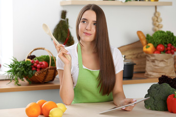 Young  brunette woman is looking a new recipe for cooking at the kitchen. Housewife holding wooden...