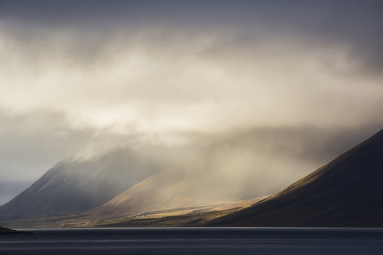 The sun shines through storm clouds in the Westfjord region; Iceland