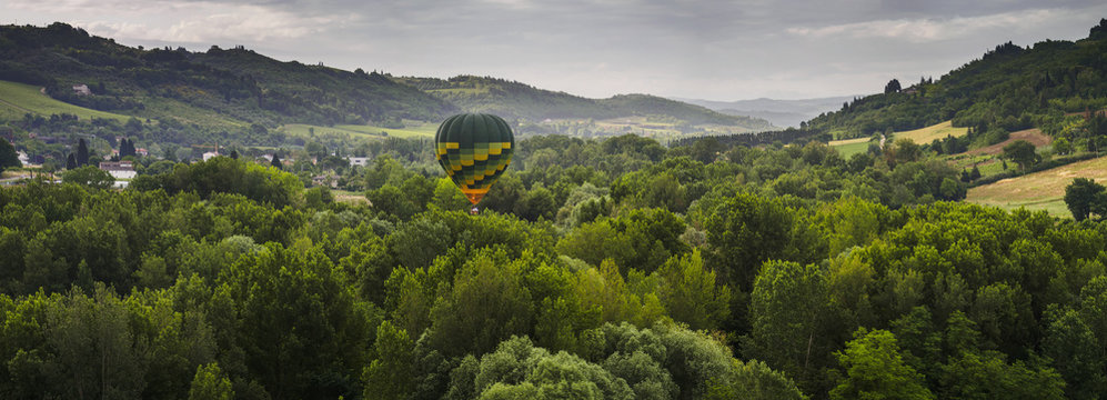 A hot air balloon flies low over a spring valley landscape; Tuscany, Italy