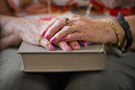 A senior woman's hands folded on a hard cover book; Devon, Alberta, Canada