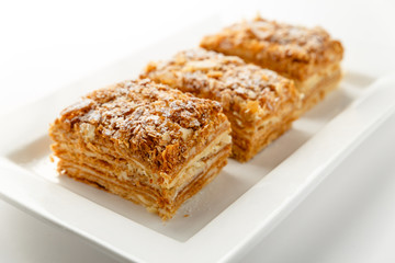 French Napoleon Cake of puff pastry with sour cream on a white plate close-up. Nutritious dessert. Selected Focus