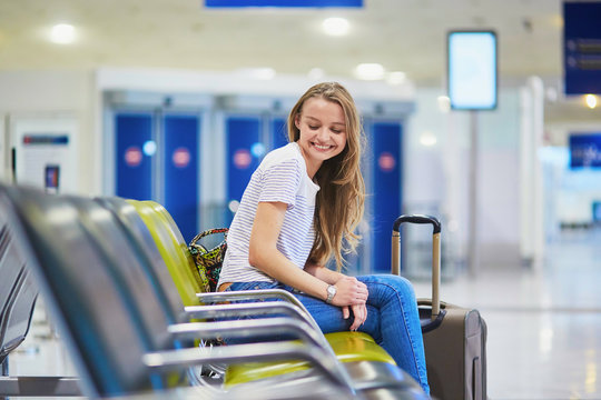 Tourist girl with backpack and carry on luggage in international airport, waiting for flight