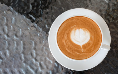 Top view of hot coffee latte art flowershape foam on glass table background