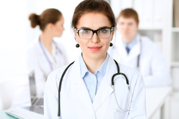 Fototapeta premium Cheerful smiling female doctor on the background with physician and his patient in the bed. High level and quality of medical service concept.