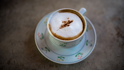 Cappuccino hot coffee on painted flower saucer in vintage style picture.