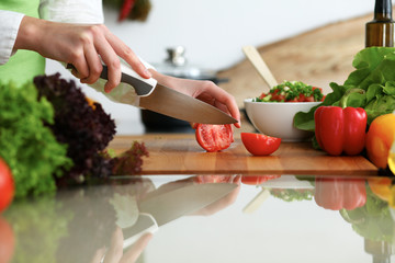 Closeup of human hands cooking vegetables salad in kitchen on the glassr table with reflection. Healthy meal and vegetarian concept