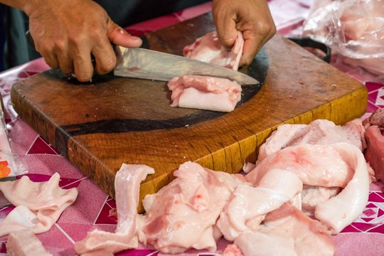 Butcher Hands Cutting Piece Of fresh Belly pork meat.
Raw pork on wooden cutting board.