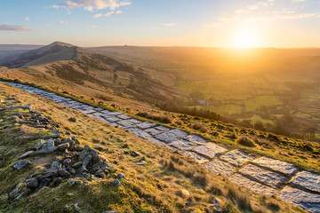 Stone walking path running along ridge of Mam Tor in the British Peak District with sun rising...