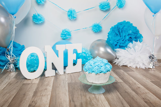 Festive background decoration for birthday celebration with gourmet cake, letters saying one and blue balloons in studio, cake smash first year concept