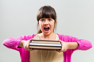 Angry little girl holding books on gray background.