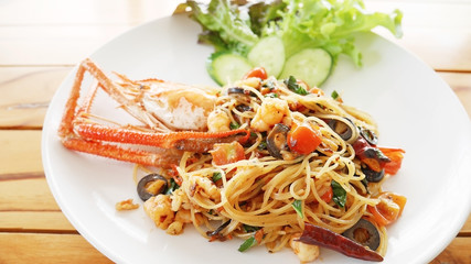 Pasta with giant prawn, olives, tomatoes, and chilli on wood background