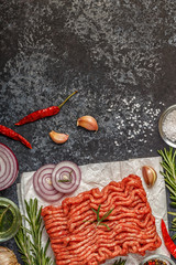 Raw minced meat on paper with onion, herbs and seasonings on black background.