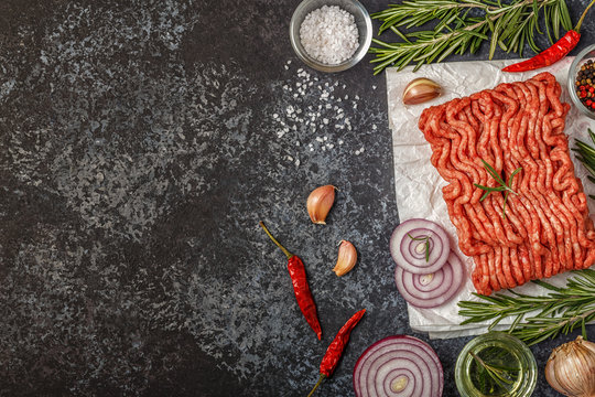 Raw minced meat on paper with onion, herbs and seasonings on black background.