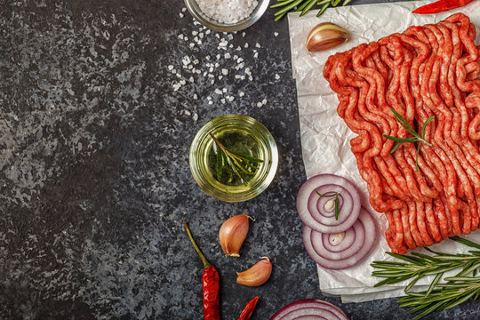 Raw minced meat on paper with onion, herbs and seasonings on black background.