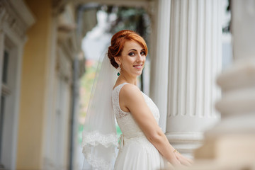Fototapeta premium Smiled red haired bride background large columns of antique house.