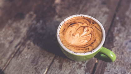 Tasty latte hot coffee in green cup on grunge wooden table vintage style.