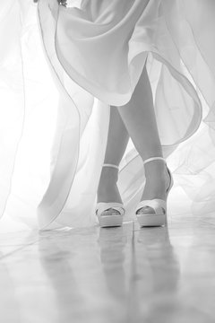 dettaglio scarpe e abito da sposa in foto bianco e nero su sfondo tenda - le gambe sono incrociate