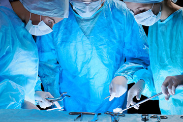 Medical team performing operation. Group of surgeon at work in operating theatre toned in blue.
