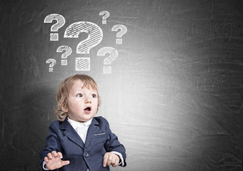 Baby boy and question marks on blackboard