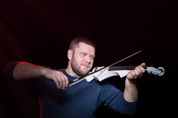 Bearded violinist plays intently on electric violin, isolated on a black background