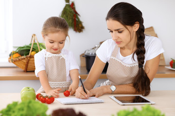 Happy family in the kitchen. Mother and child daughter make menue for cooking tasty breakfest in the kitchen