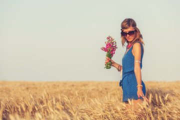 Girl holding flower bouquet in wheat field.