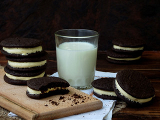 Homemade chocolate cookies with white marshmallow cream and glass of milk on dark background. Selective focus.