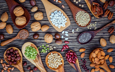 Various legumes and different kinds of nutshells in spoons. Walnuts kernels ,hazelnuts, almond ,brown pinto ,soy beans ,flax seeds ,chia ,chickpea ,red kidney beans and pecan on shabby wooden table.