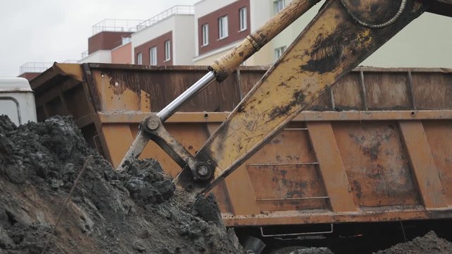 Close up slowmotion excavator bucket dig soil and dump in to back of truck at building site