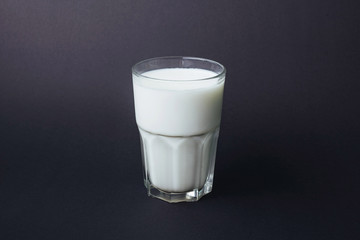 Transparent glass of milk on a black background.