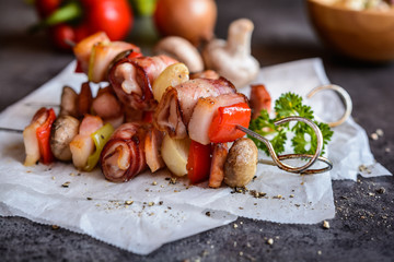 Grilled skewers with rabbit meat wrapped in a bacon with onion, mushrooms and pepper