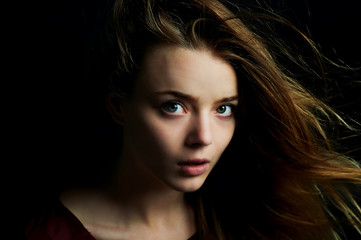 Beautiful girl looks piercing eyes into the camera. Hair flying. Drama. Studio photography in low...