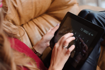 Close-up of the hands of a young woman working with the tablet and the calculator