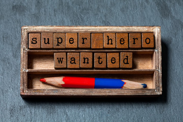 Super hero wanted phrase. Recruiting and personal searching concept quote. Vintage box, wooden cubes with old style letters, red blue pencil. Gray textured background. Close-up, up view, soft focus.