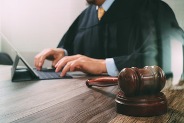 justice and law concept.Male judge in a courtroom with the gavel,working with digital tablet computer docking keyboard on wood table,filter effect