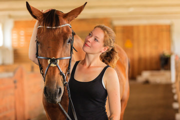 Jockey young girl petting and hugging brown horse