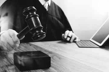 justice and law concept.Male judge in a courtroom striking the gavel,working with digital tablet computer docking keyboard on wood table,black and white