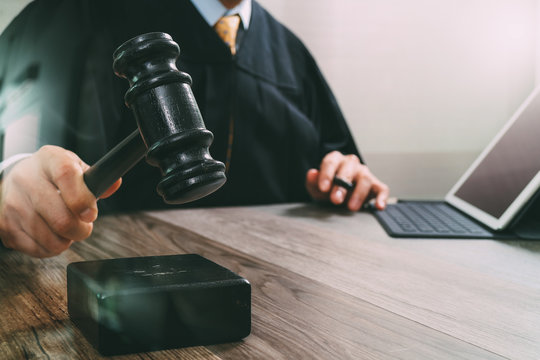justice and law concept.Male judge in a courtroom striking the gavel,working with digital tablet computer docking keyboard on wood table,filter effect