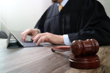justice and law concept.Male judge in a courtroom with the gavel,working with digital tablet computer docking keyboard on wood table