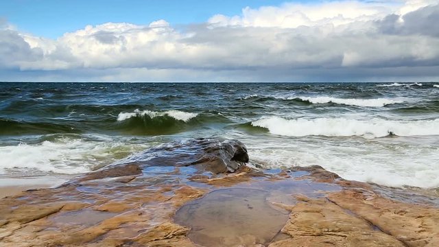 Lake Superior waves roll in against a rocky coast under a cloudy blue sky at Pictured Rocks National Lakeshore in the upper Peninsula of Michigan in this seamlessly looping video footage.