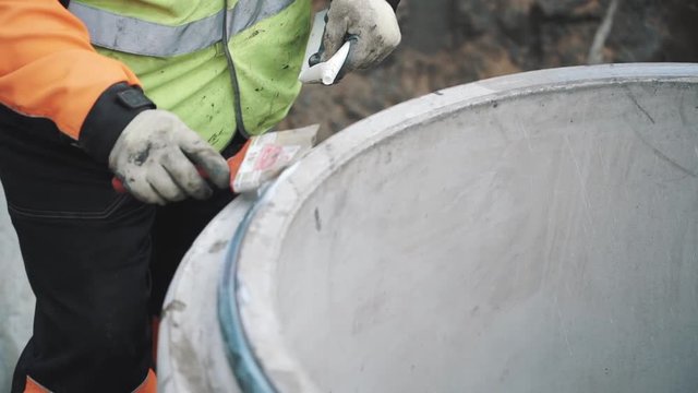 Builder put white glue on edge of concrete manhole ring with brush. Slowmotion, close up