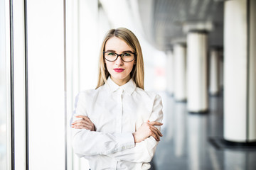 Portrait of blonde business woman with crossed hands in modern office.
