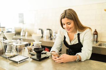 Female barista using a smartphone at work
